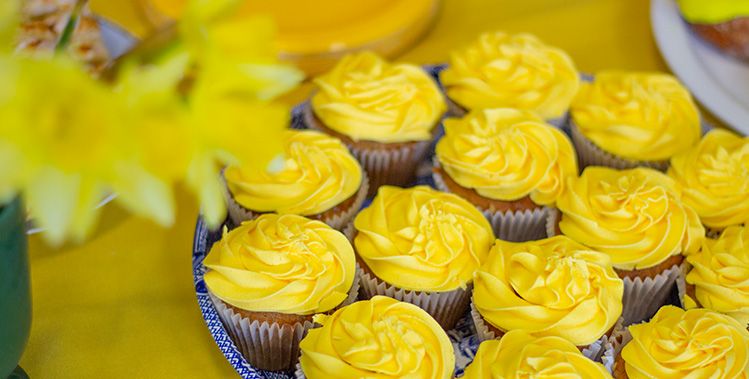 Cupcakes with yellow icing on a serving platter resting on a yellow tablecloth