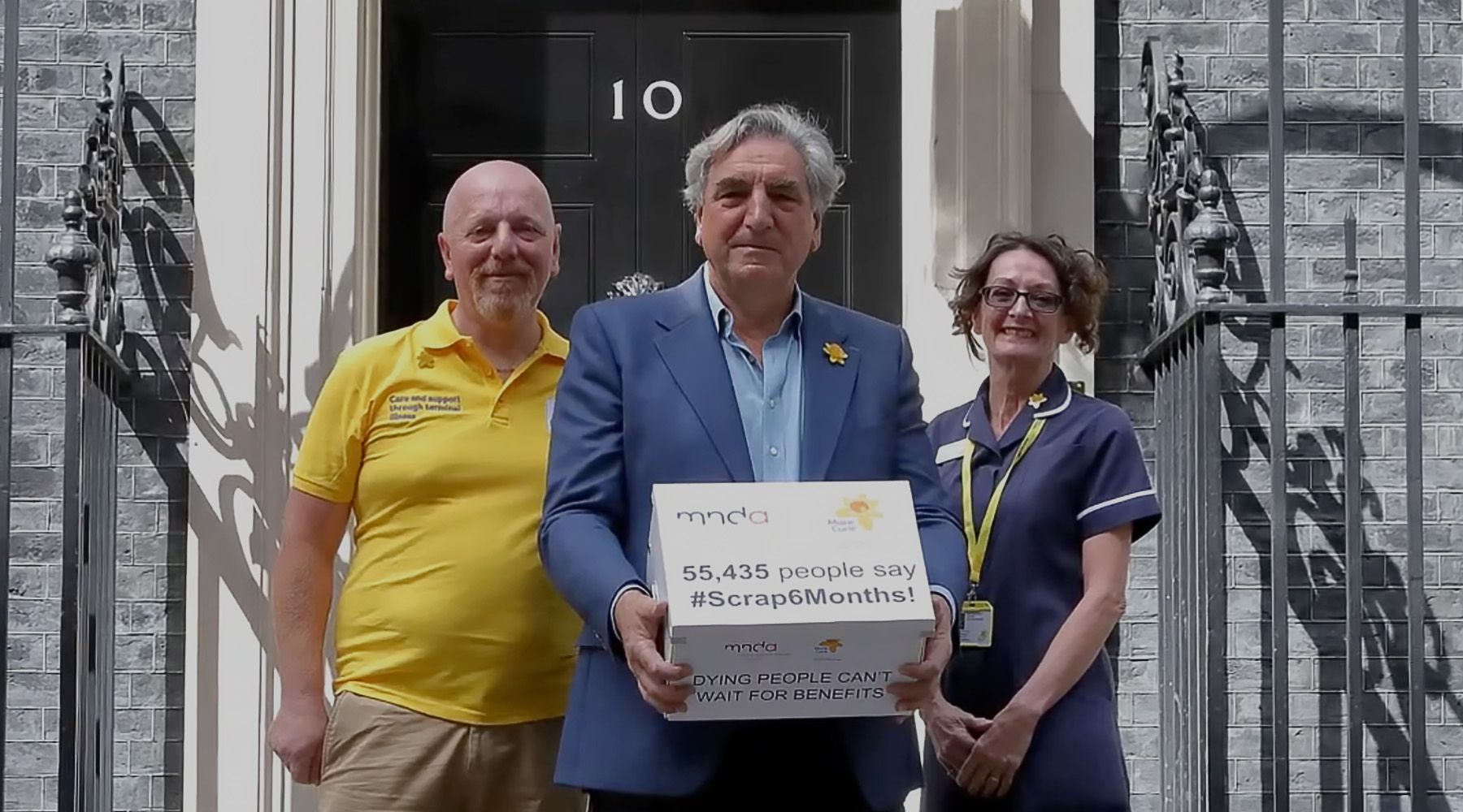 Campaigner holding banner outside Downing Street saying 'Cut the red tape for people living with a terminal illness #Scrap6Months'