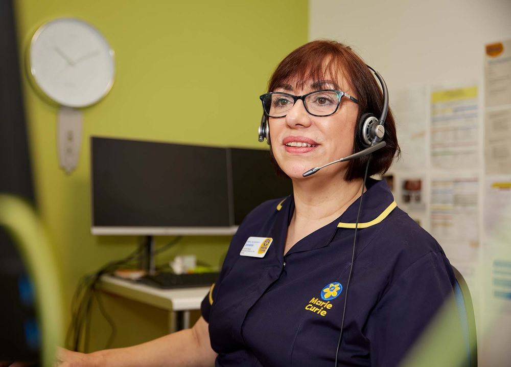 A Support Line Officer in Marie Curie uniform takes a Support Line call on a phone headset.