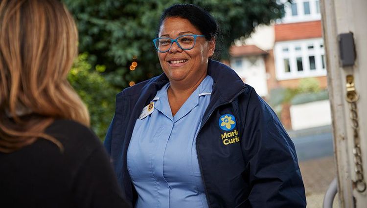 Marie Curie Nurse smiles while she speaks to a woman in the doorway of a home