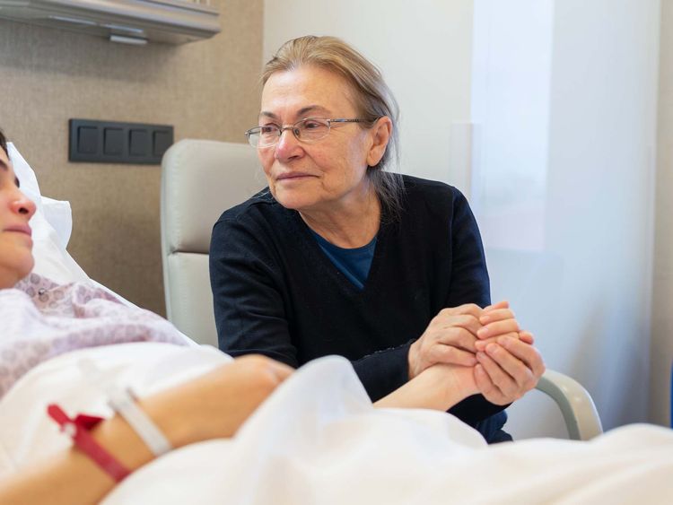 Companion holding patient's hand in hospital by bedside