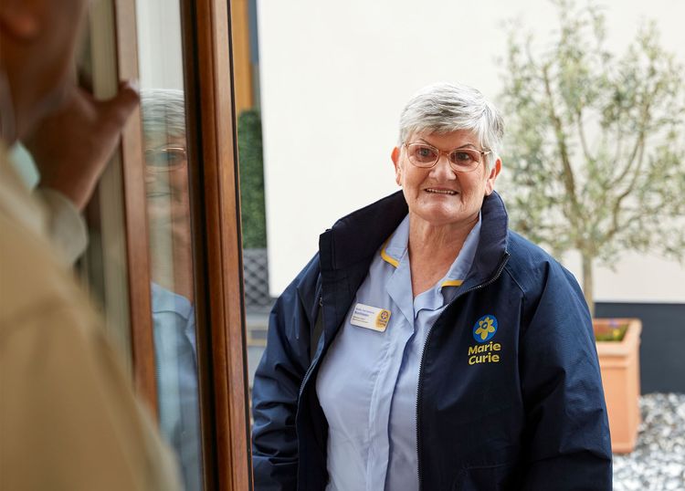 A Marie Curie Nurse stands in the doorway of a person's home.