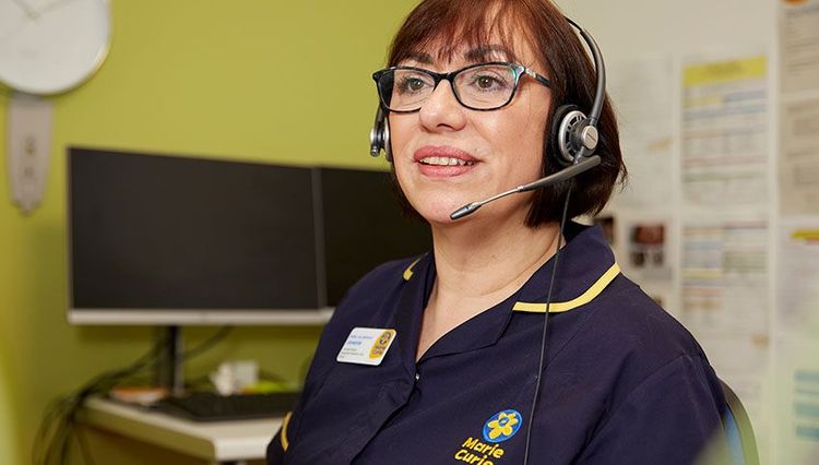 A woman with a headset is talking on the phone. She's sat at a desk and a desktop is visible behind her.