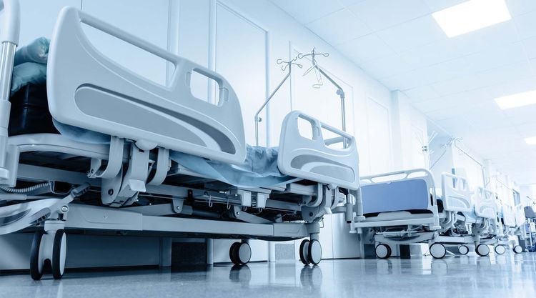 Empty hospital patient beds lined up against a wall 