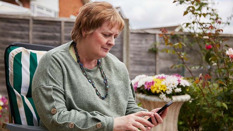 A woman sits outside in her garden as she looks at her mobile phone.