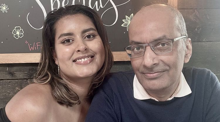 A young woman and her father sit aide by side and smile at the camera