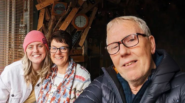 A man smiles as he takes a selfy with two women also smiling