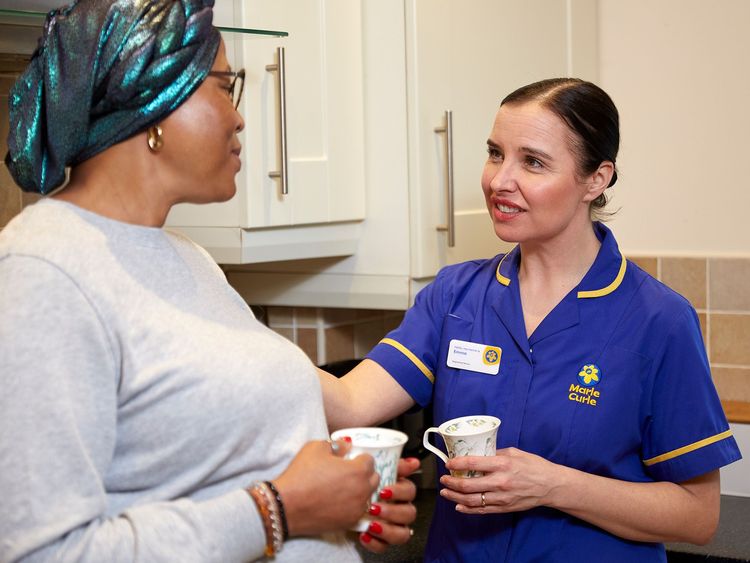 A Marie Curie Nurse talks to a patient while sharing a cup of tea
