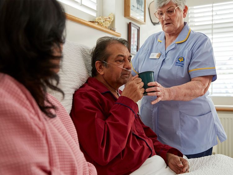 A Marie Curie Healthcare Assistant cares for a man sitting up in bed
