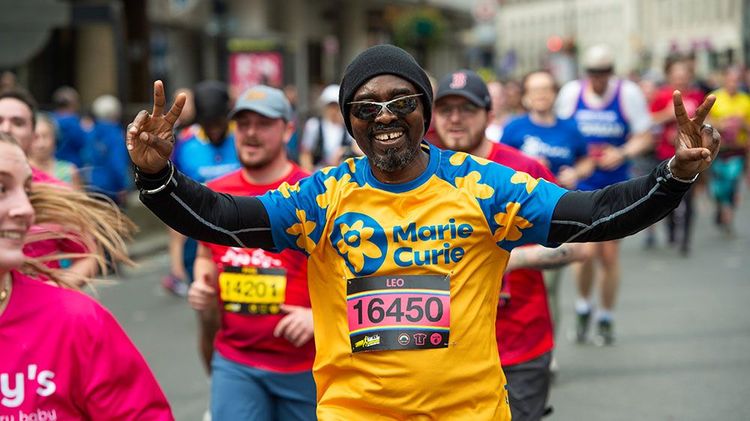 Man holds his arms up and smiles as he poses for a photograph while he runs in a marathon