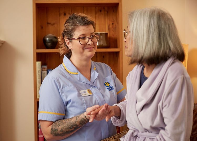 A Marie Curie Nurse stands next to a patient and holds her hand