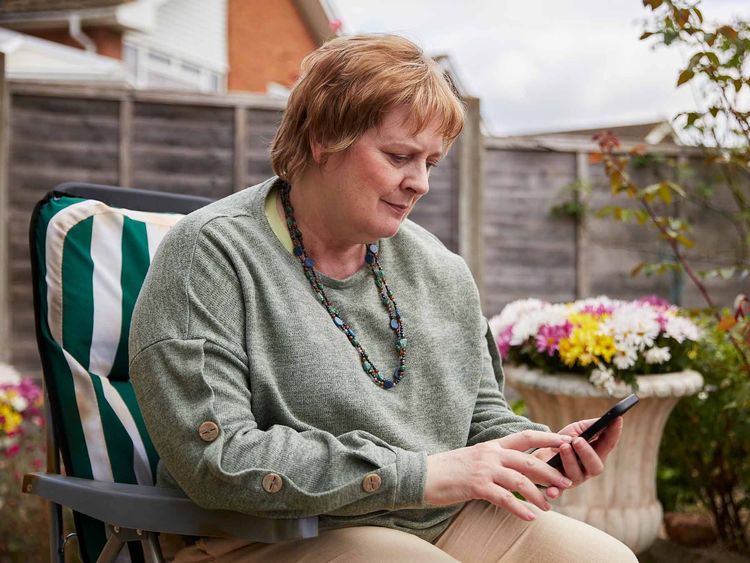 A woman sitting outdoors types into her mobile phone as she has an online chat with the Marie Curie Support Line.