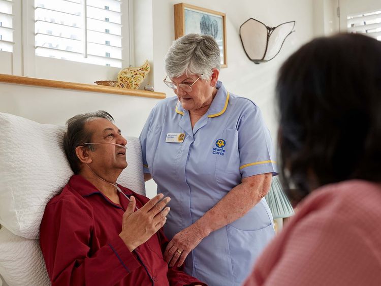 A Marie Curie Nurse stands and speaks to a seated patient