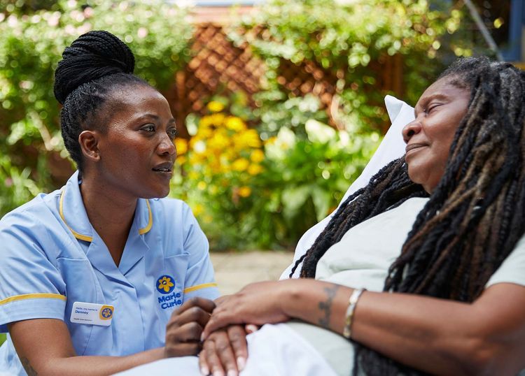 A Marie Curie Nurse sits next to a patient in their hospice bed. 